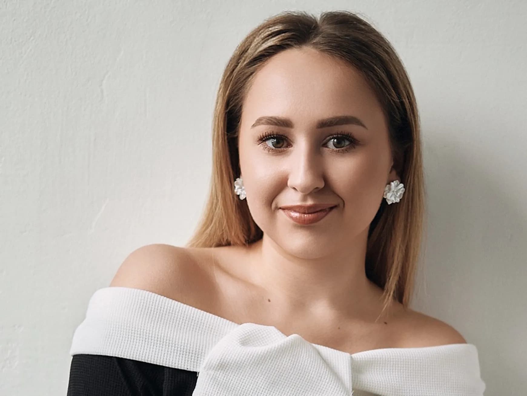 Жінка зі світлим волоссям у чорній сукні з білим бантом на рівні плечей