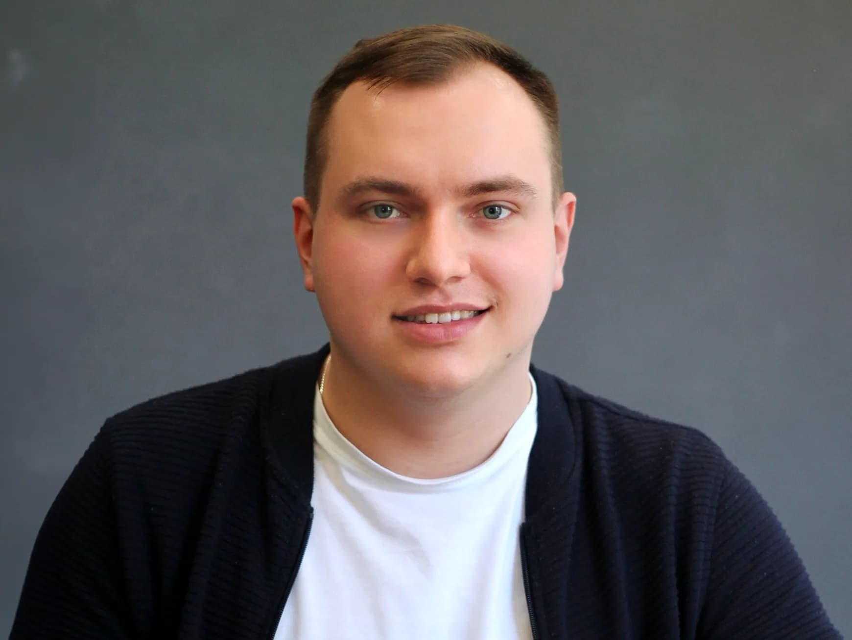 Чоловік з темно-русявим волоссям у білій футболці і темно-синьому кардигані