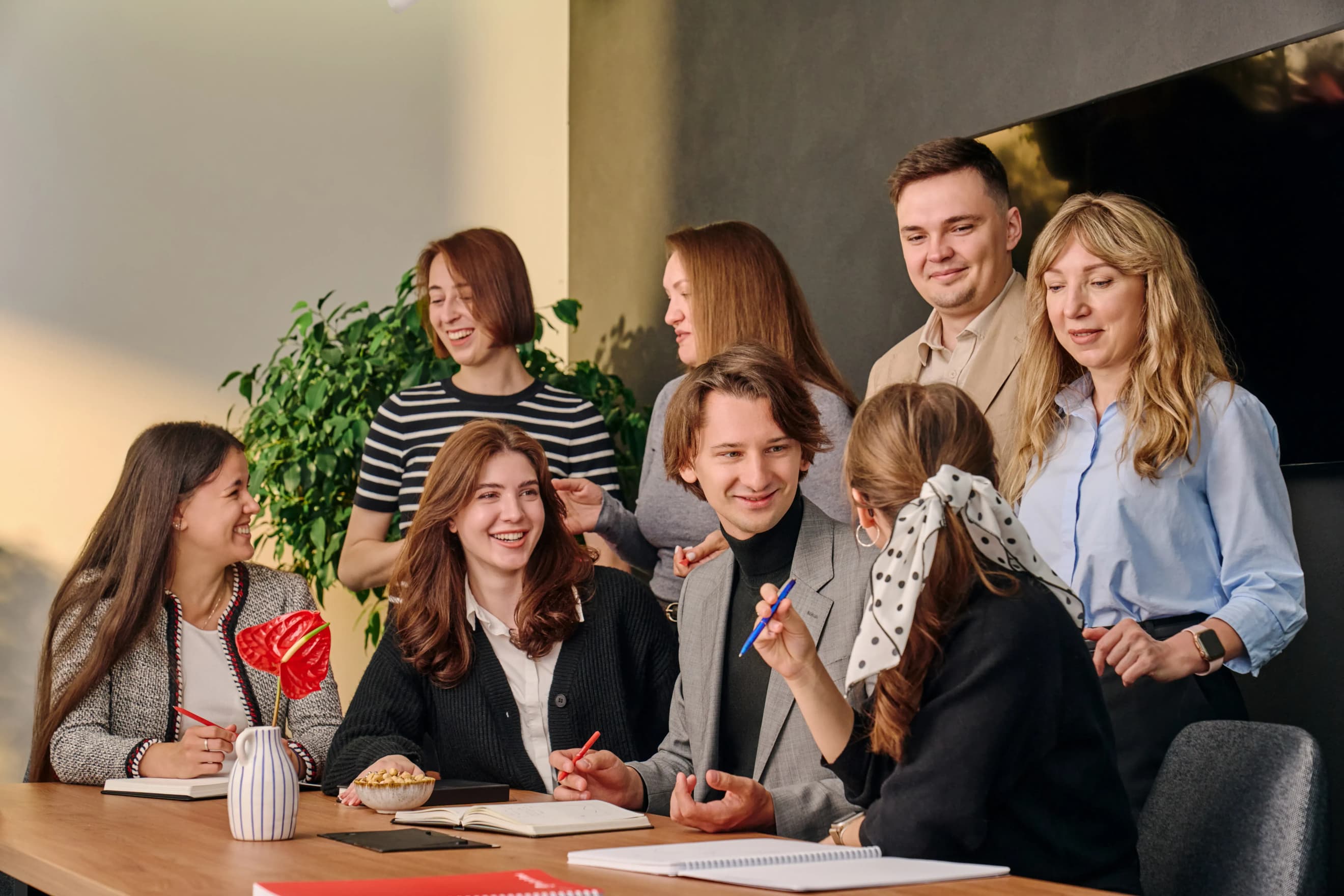 Група людей зібралась навколо столу з блокнотами і ноутбуками та веде активне обговорення