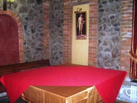 Зал з кам’яною стіною, подіумом і столом, накритим червоною скатертиною