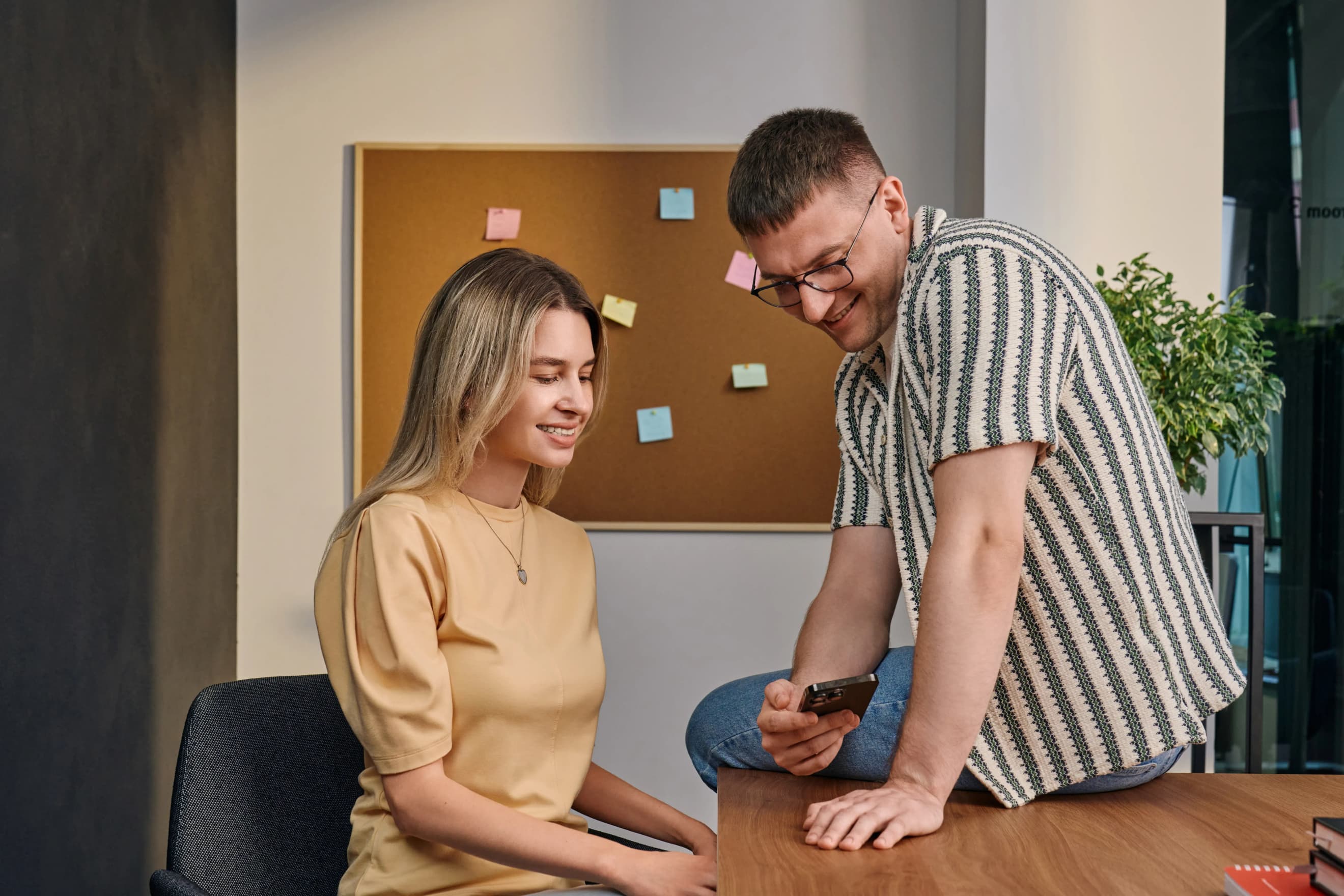 Двоє людей біля столу обговорюють інформацію на смартфоні, сидячи поруч у робочому просторі