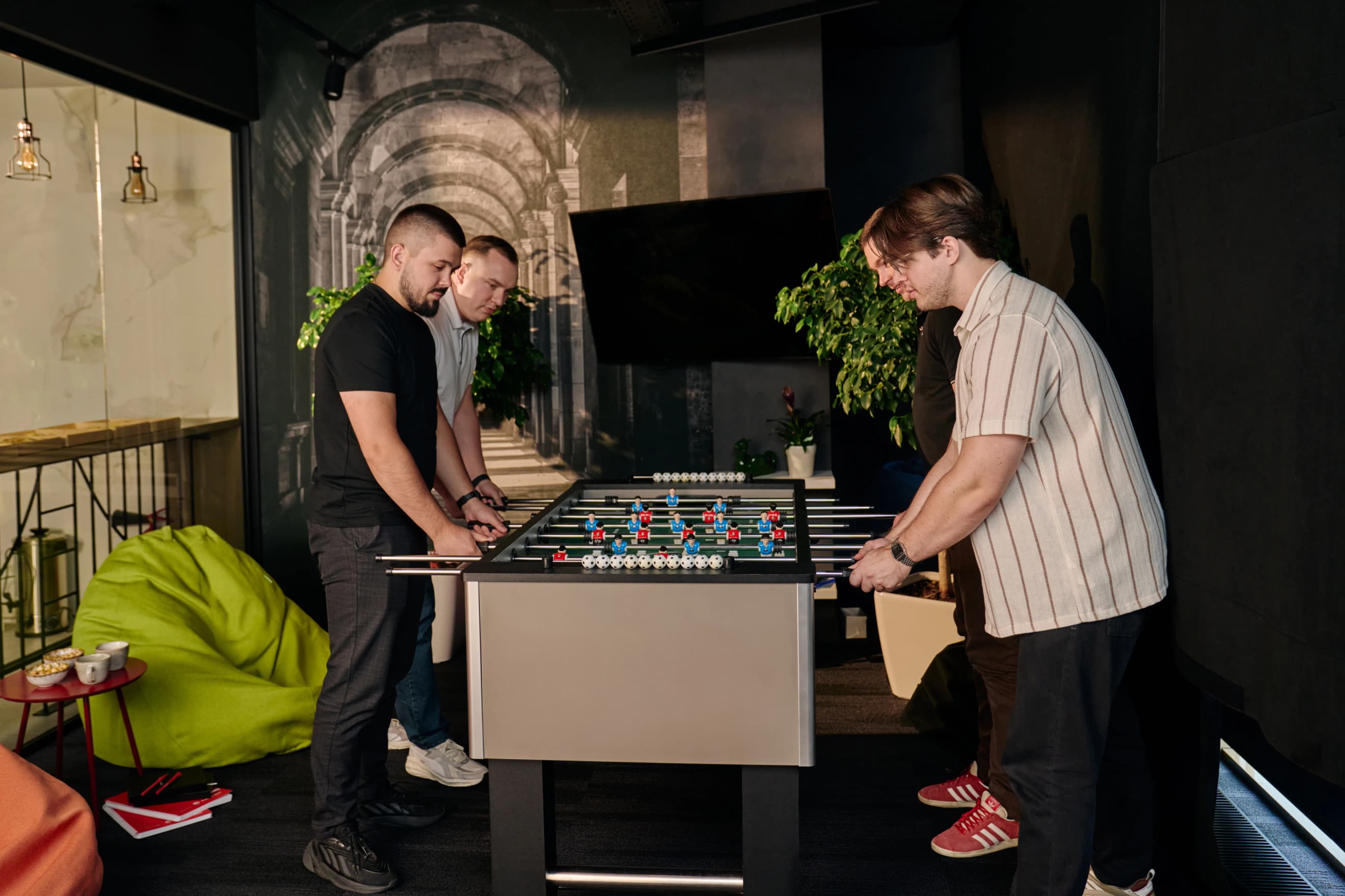 Четверо чоловіків грають у настільний футбол у зоні відпочинку офісу