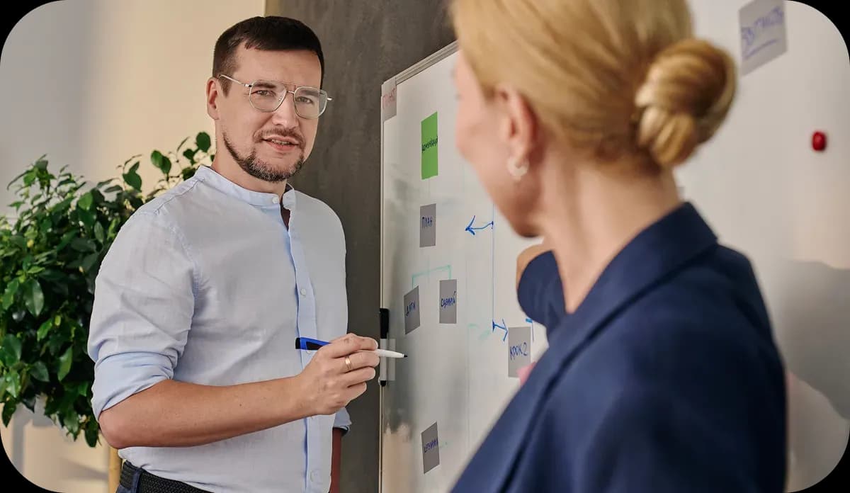 Двоє людей обговорюють схему на дошці з наліпками та стрілками