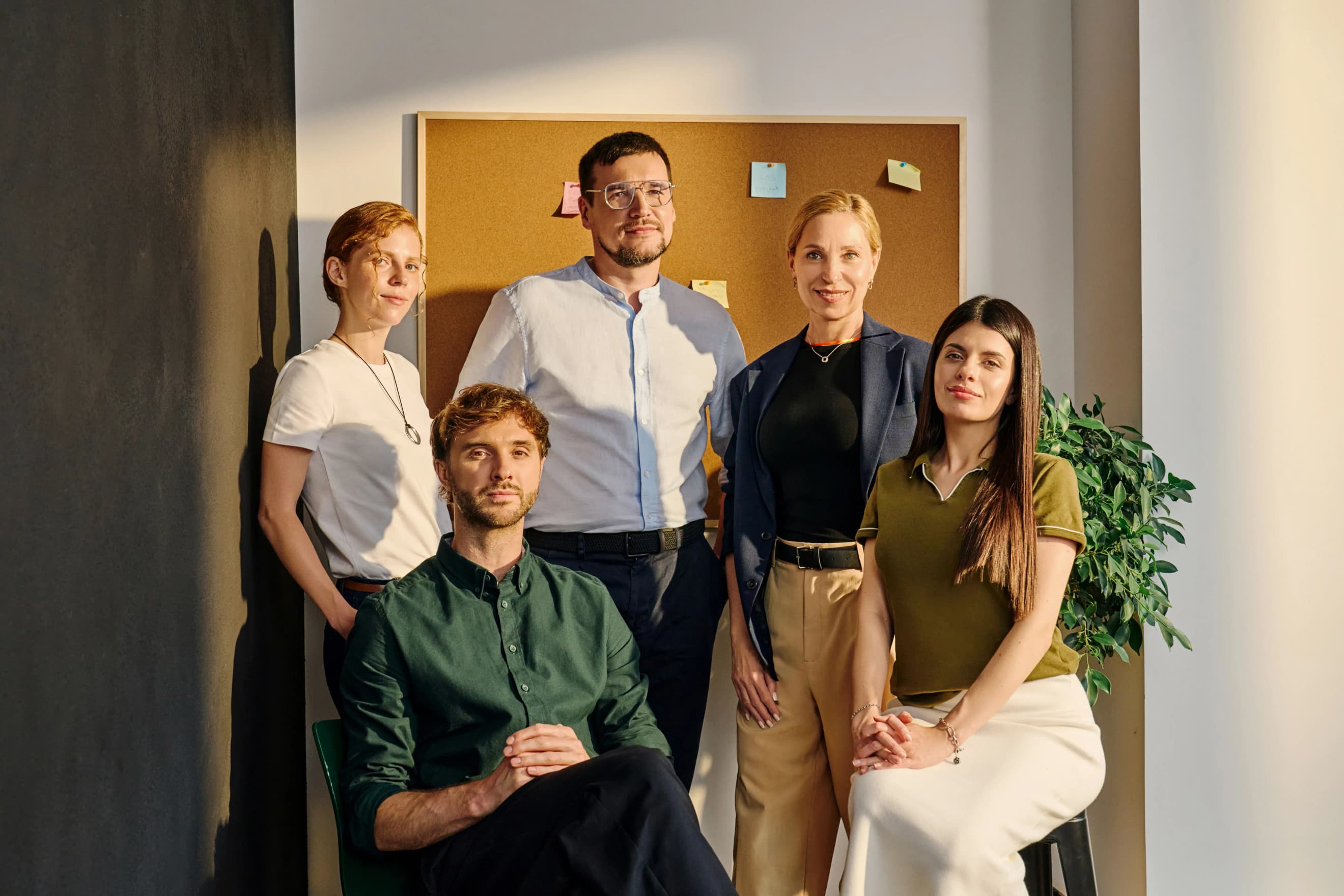 Група людей позує для фото в офісі перед корковою дошкою з різнокольоровими наліпками