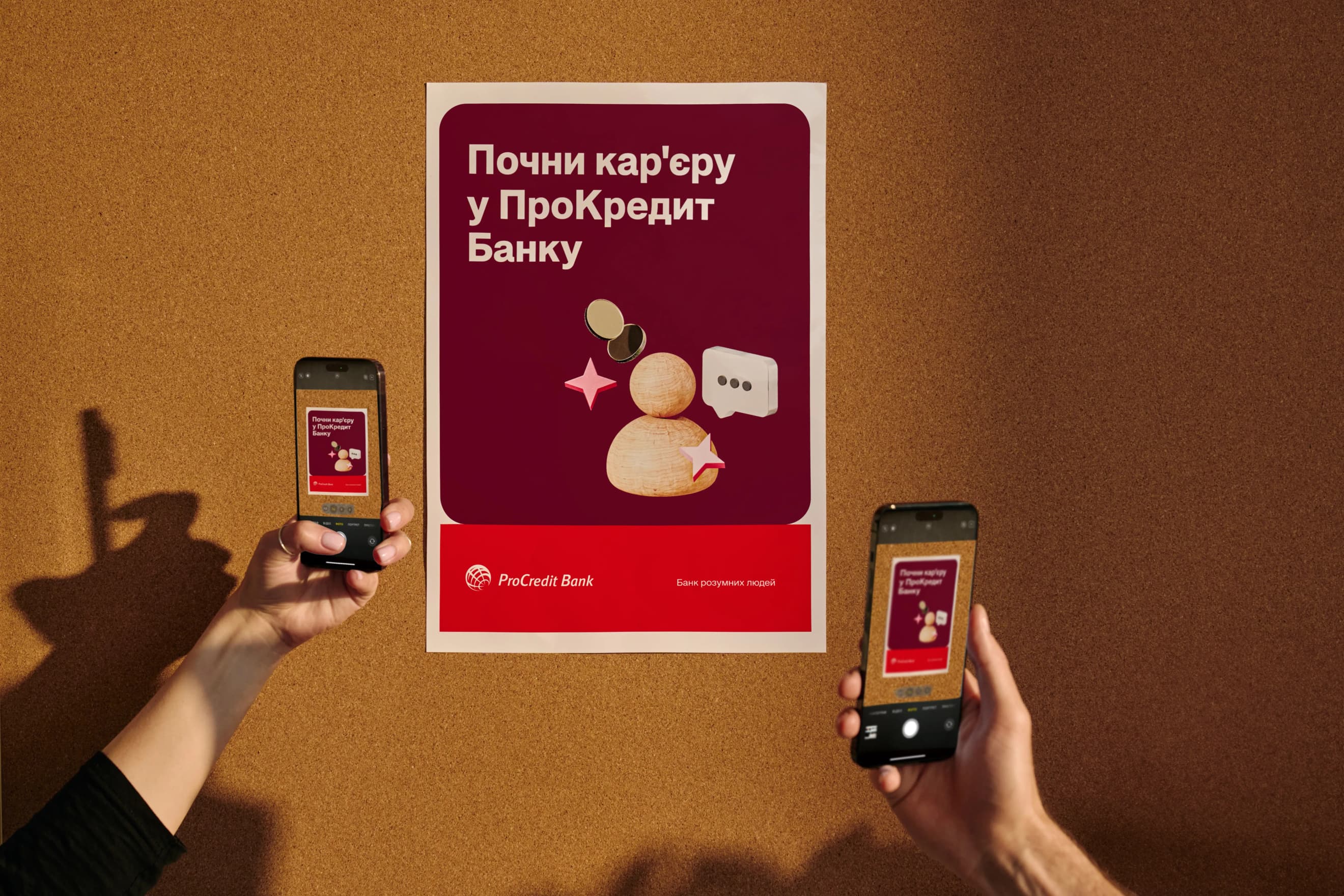 Дві руки тримають смартфони, знімаючи плакат про кар’єрні можливості в банку на корковій дошці