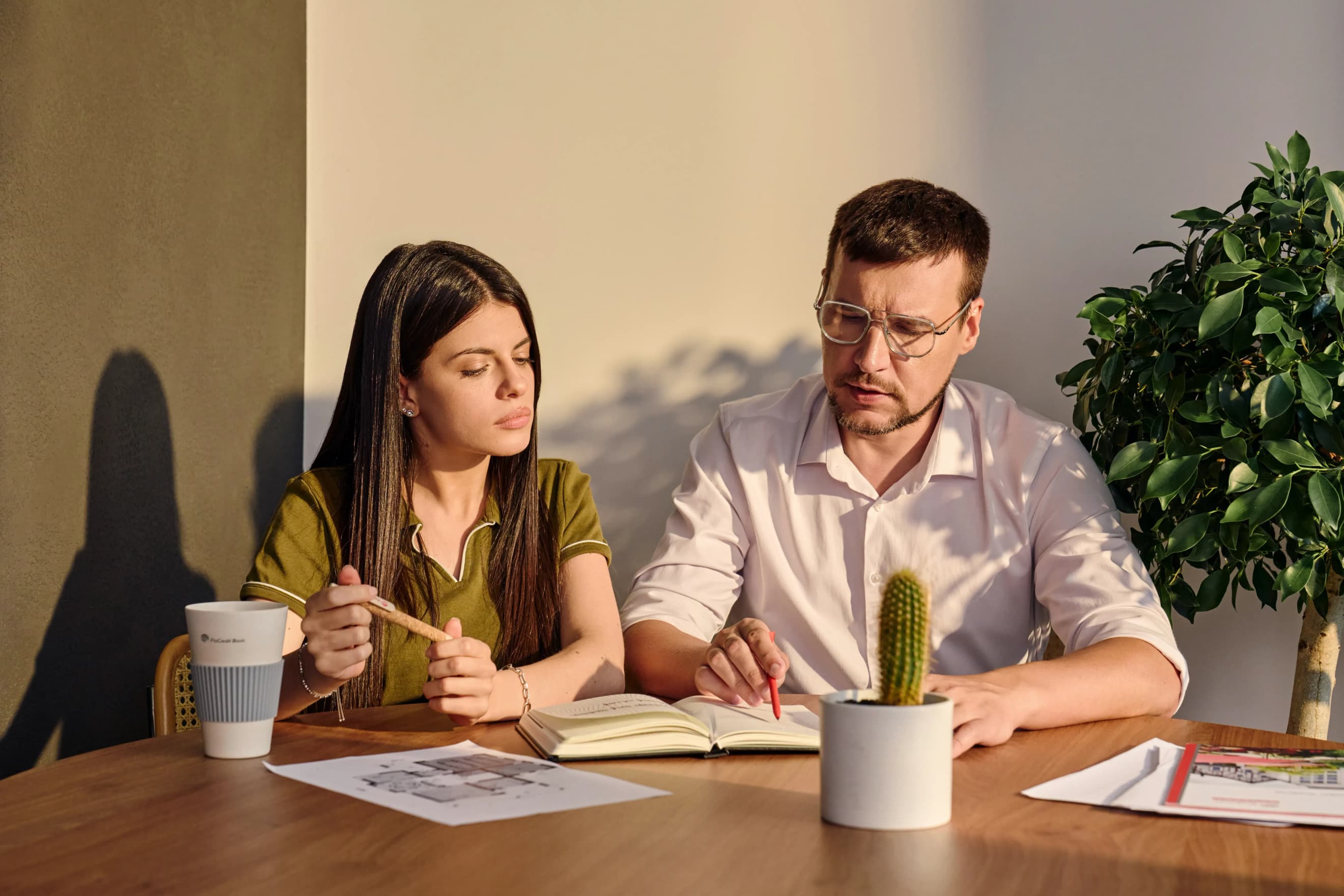 Жінка та чоловік сидять за столом, роблять нотатки в блокноті та переглядають документи поруч із рослиною