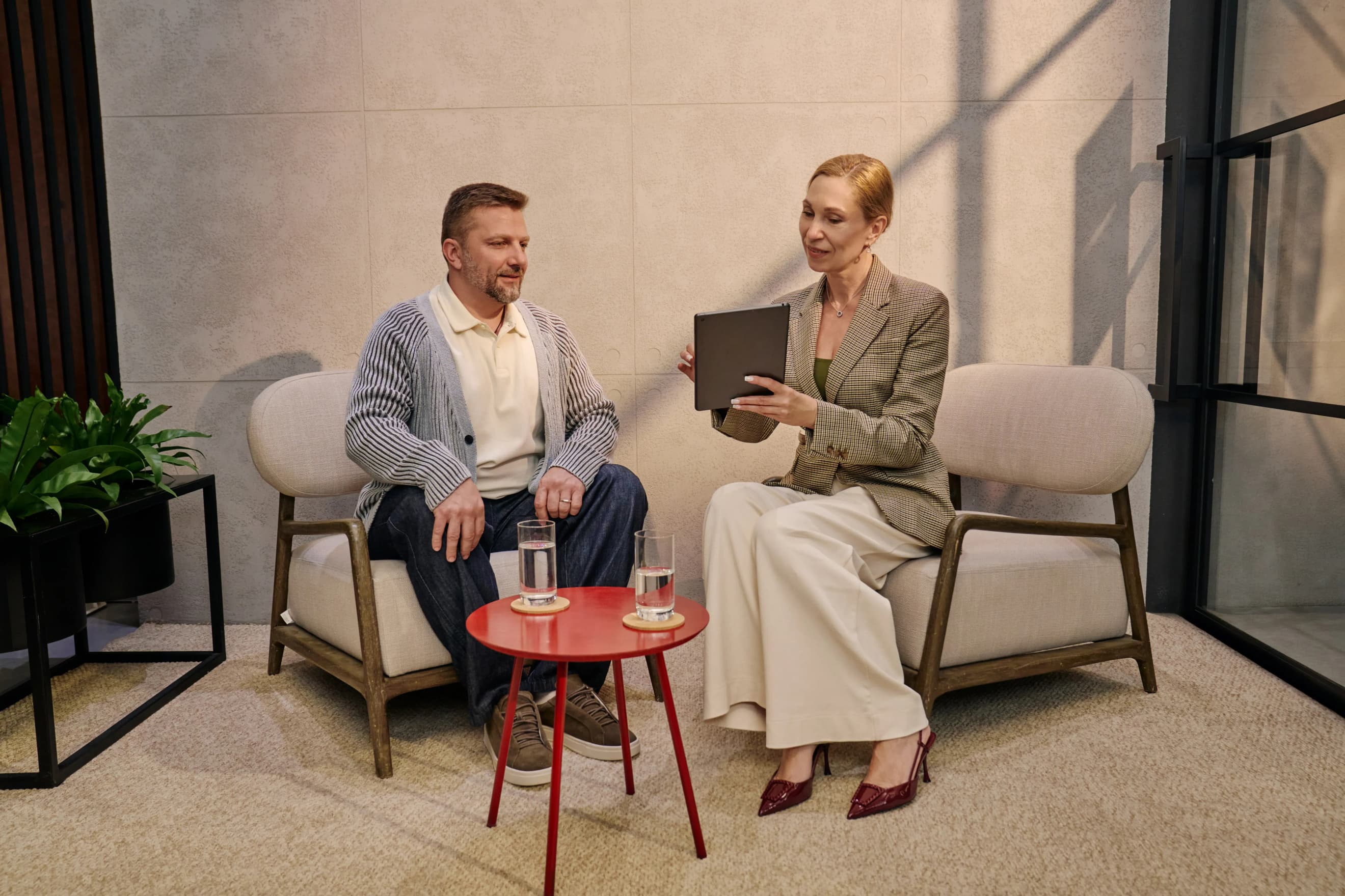 Чоловік та жінка сидять у лаунж‑зоні на кріслах, обговорюючи інформацію на планшеті за невеликим столиком з водою