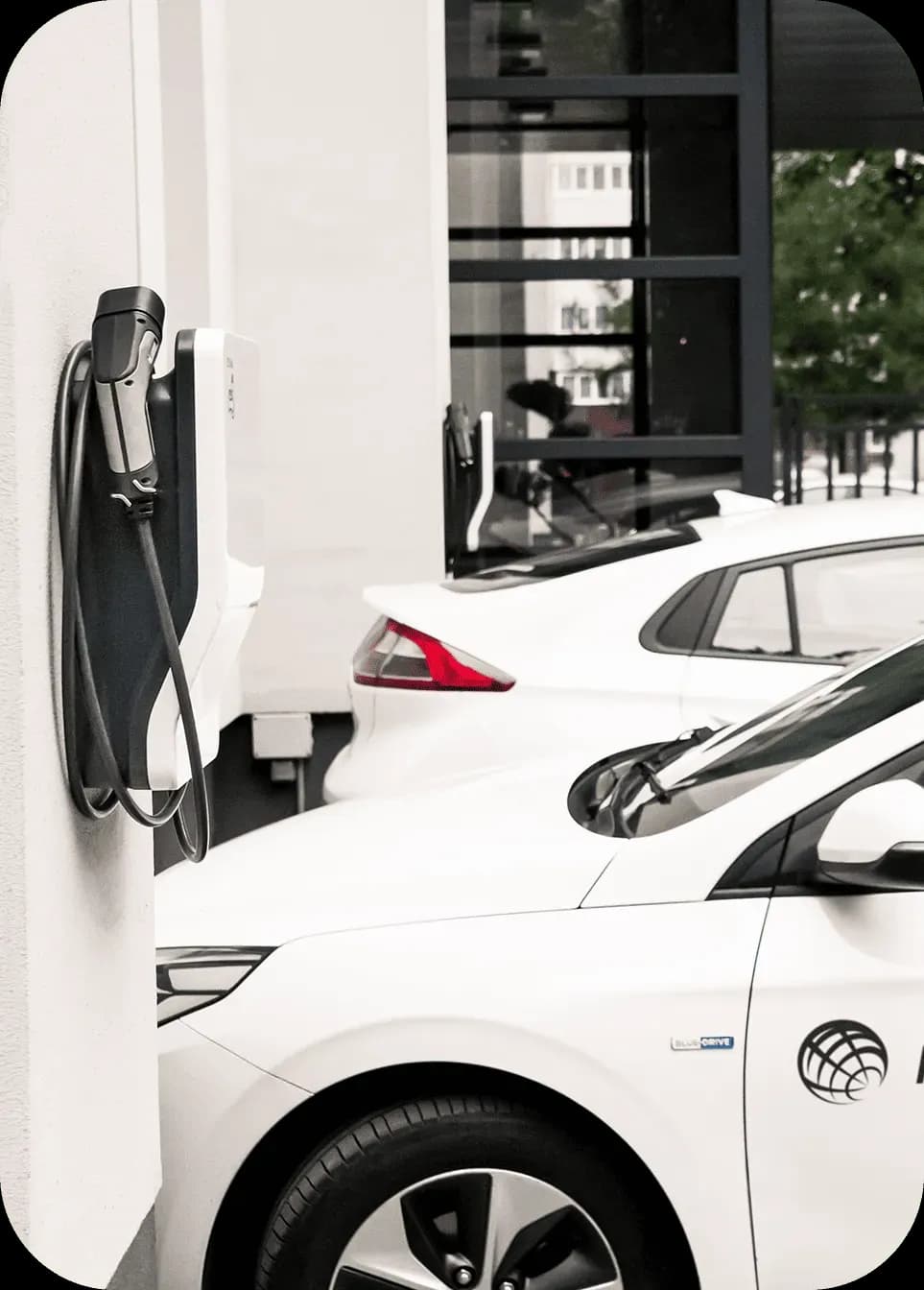 Електромобілі припарковані біля зарядної станції, кабель зарядки закріплений на стіні поруч