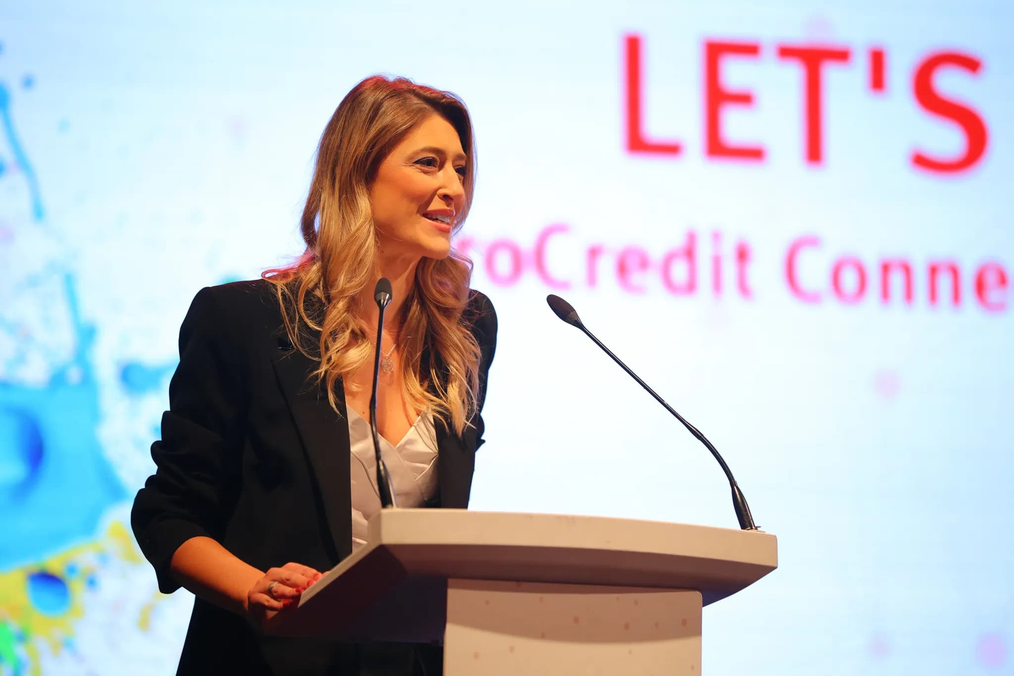 Жінка стоїть за трибуною з мікрофонами під час виступу на події ProCredit Connect