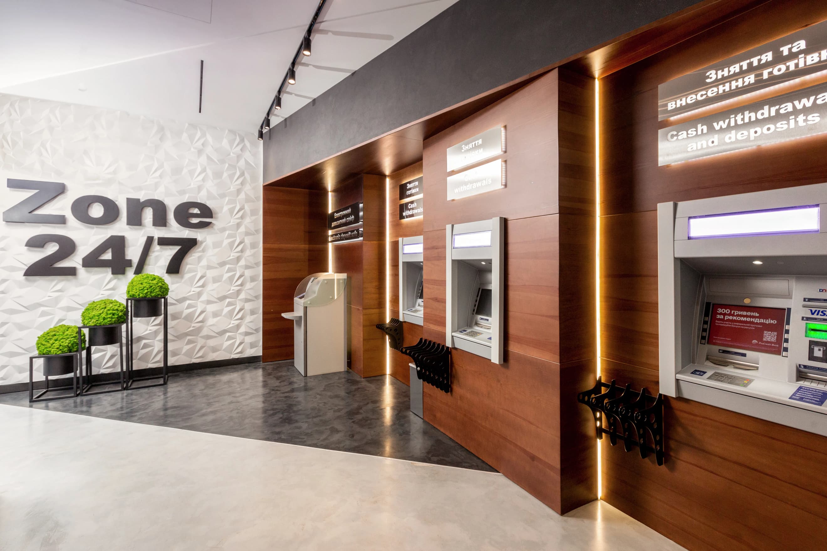 Цілодобова зона у відділенні банку з рядом банкоматів та декоративними рослинами у сучасному інтер’єрі